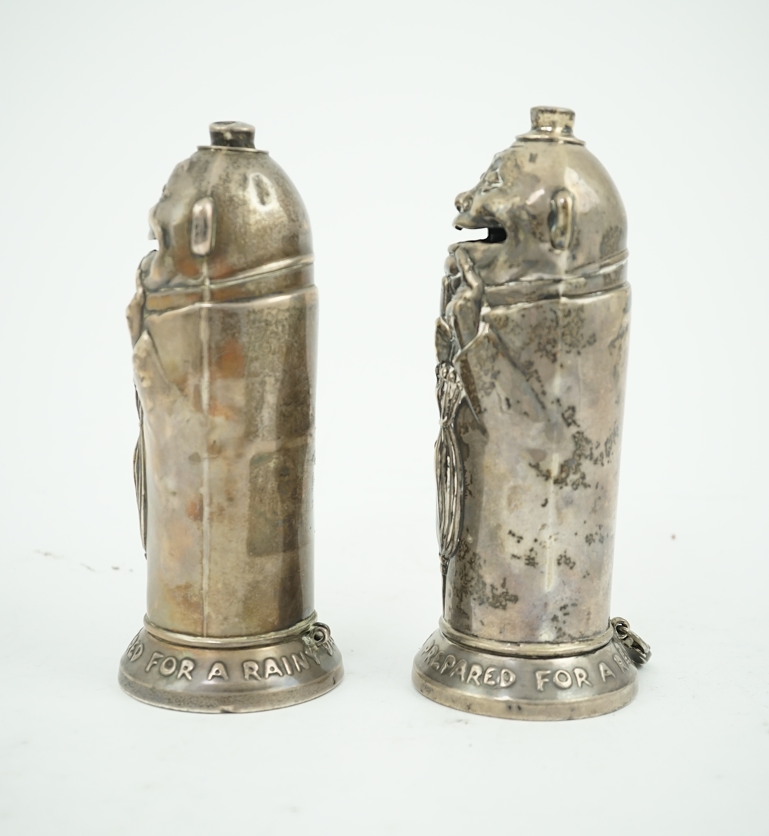 A matched pair of George V novelty silver money boxes, each cylindrical box embossed as a banker with an umbrella, the circular base inscribed 'Always be prepared for a rainy day'